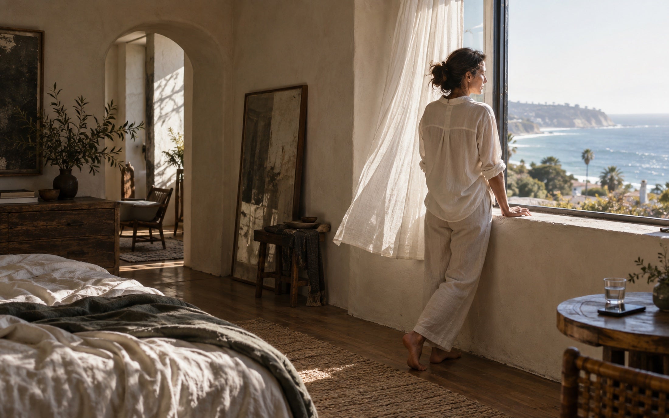 A woman takes a quiet pause beside an open window in morning light.